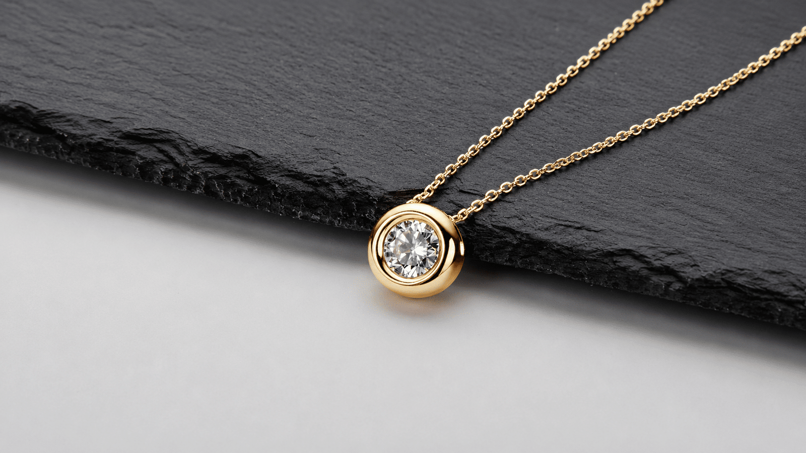 Gold-tone moissanite pendant necklace displayed on black slate in a 16:9 composition.